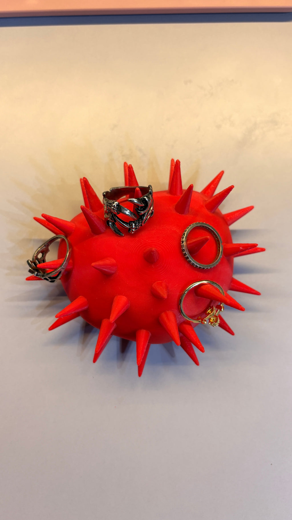 Silver rings displayed on the spikes of a red 3D printed goth heart ring stand.