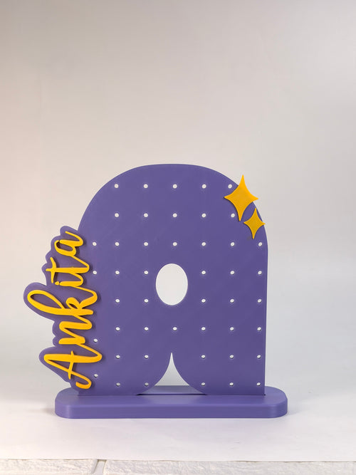 Custom 3D printed purple letter A earring holder with the name Ankita written in yellow script on the side.
